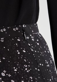 Gonna nera in tessuto con motivo floreale bianco e pieghe, dotata di una chiusura a zip discreta e una vita testurizzata.