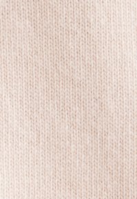 Gros plan d’un tissu tricoté beige doux montrant des points de tricot détaillés et une texture dans un motif vertical régulier.