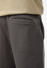 Grå sweatpants med en glat tekstur og en sidelomme med en diskret åbning. Kombineret med en lys T-shirt.