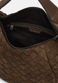 Brązowa pleciona skórzana torebka z otwartym suwakiem na górze, ukazująca czarną materiałową wyściółkę i wewnętrzną kieszeń na zamek.