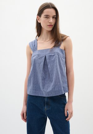 Haut sans manches bleu clair avec un décolleté carré, un devant plissé et un tissu texturé. Associé à un jean bleu foncé.