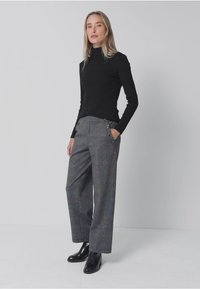 Czarna bluzka z długim rękawem w połączeniu z szarymi spodniami szerokimi w kratę, które mają boczne kieszenie i guziki. Uzupełniona czarnymi botkami za kostkę.