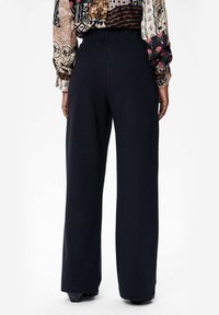 Wijdvallende broek in donkerblauw, met een gladde textuur en hoge tailleband. De achteraanzicht toont recht gesneden benen en minimale details.