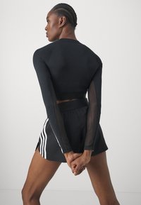 Crna atletska kratka majica s dugim mrežastim rukavima, u kombinaciji s crnim šortsem s bijelim prugama i bočnim prorezima. Slim fit dizajn.