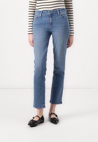 Jeans de denim azul claro con corte recto, con una cintura de altura media y un dobladillo limpio, combinados con zapatos planos negros adornados con ojales decorativos.