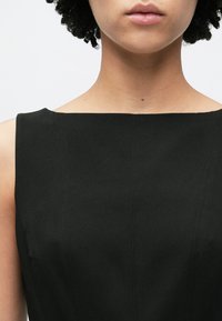 Μαύρο αμάνικο φόρεμα με τετράγωνο ντεκολτέ, με λεία υφή και καθαρές γραμμές. Λεπτή ραφή ορατή στο ύφασμα.