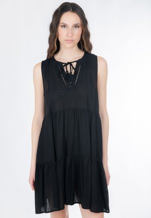 Schwarzes ärmelloses Kleid mit Rundhalsausschnitt, Bindedetail vorne und strukturierten Stufen. Hergestellt aus leichtem Stoff, fällt über das Knie.