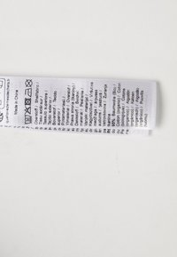 Oznaka od bijelog platna koja sadrži upute za njegu, informacije o materijalu i simbole za pranje ispisane na više jezika.