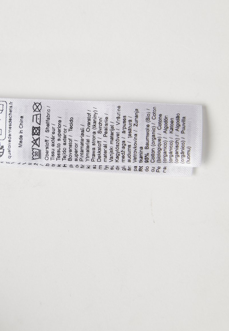 Oznaka od bijelog platna koja sadrži upute za njegu, informacije o materijalu i simbole za pranje ispisane na više jezika.