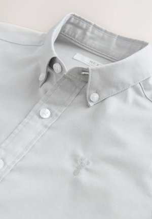 Helehall halli särgi, millel on klassikaline krae, valged nööbid ja ees väike tikitud detail.