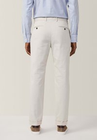 Witte broek met een rechte pasvorm, voorzien van twee achterzakken, twee voorzakken en omgeslagen pijpen, gecombineerd met bruine schoenen en een gestreept shirt.
