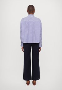 Blå och vitrandig skjorta med avslappnad passform, långa ärmar och manschettdetaljer; kombinerad med högmidjade, marinblå vida byxor.