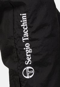Zwarte sportjas met een gekreukt textuur. De merknaam "Sergio Tacchini" is in het wit geborduurd langs de zijkant, samen met een cirkelvormig logo.