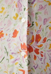 Țesătură cu modele florale în culori pastelate, având accente roșii, galbene și verzi. Include un detaliu cu un nasture alb pe partea stângă.