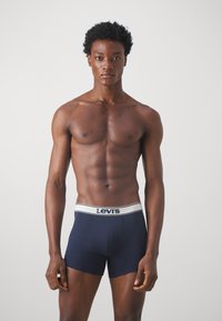 Tamno plave bokserice s bijelim Levi's logom, prilagodljiv dizajn, elastična tkanina i ravni šavovi, nosi ih model.