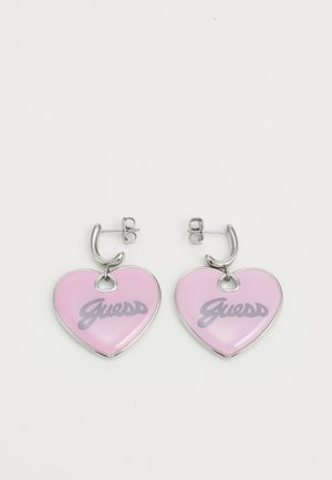 Silberne Creolen mit rosa herzförmigen Anhängern, jeder mit dem Wort „Guess“ in grauer Schrift graviert.