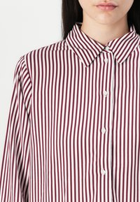 Maroon and white striped shirt with a pointed collar, front button closure, and long sleeves, featuring a soft fabric texture.