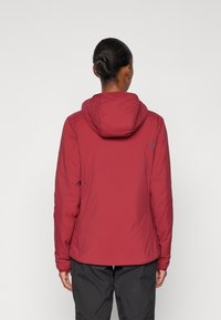 Veste isolante rouge avec capuche, en matériau léger, poignets élastiques et détail de logo discret au dos. Conçue pour la chaleur et la mobilité.