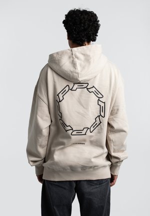 Beige hoodie with a large black circular graphic on the back, made of soft material, featuring a drawstring hood and oversized fit.