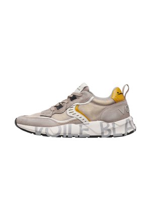 Beige und gelber Velours- und Stoffsneaker mit dicker weißer Sohle, großem grauem Text und schwarzen Ösen.
