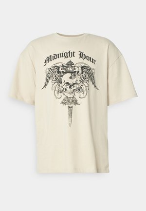 T-shirt oversize couleur crème avec un graphique noir d'un crâne, des ailes et des fleurs, portant le texte "Midnight Hour" au-dessus du design.