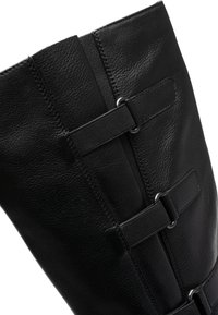 Bota de cuero negro con textura lisa, que presenta dos correas horizontales y detalles metálicos. Diseño estructurado con una caña alta.