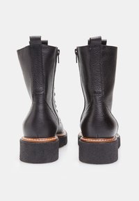 Botas de tobillo de cuero negro con un acabado texturizado, cremalleras traseras y una suela gruesa de fieltro negro. Unas costuras en contraste delimitan la entre suela color marrón claro.