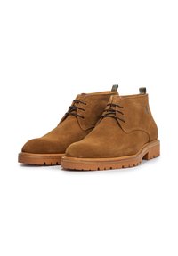 Bottines en suede marron avec un design à lacets, dotées d'une semelle en caoutchouc épaisse et d'une petite boucle en tissu à l'arrière. Texture lisse et bout rond.