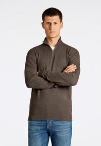 Maglione zip-up grigio scuro con colletto alto, realizzato in una texture morbida, abbinato a jeans azzurri in un semplice ambiente da studio.