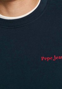 Sudadera azul marino hecha de tejido acanalado, con un escote redondo y un logo bordado en rojo "Pepe Jeans" en la parte frontal.