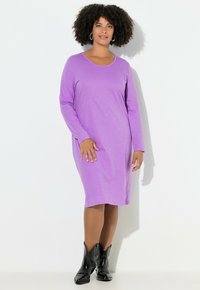 Fialové šaty s dlouhým rukávem a kulatým výstřihem, vyrobené z měkké látky, lehce volný střih, doplněné černými kovbojskými botami.