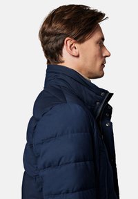 Granatowa kurtka puchowa z wysokim kołnierzem, widoczną pikowaną fakturą i zapięciem na zamek błyskawiczny z przodu. Posiada metalowe elementy i boczne kieszenie.