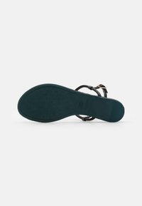 Sorte sandaler med en teksturert såle, tynne stropper og en gullspenne. Sålen har et mønstrete grepdesign og en svakt buet form.