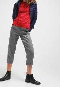 Szare, krótkie spodnie o delikatnej teksturze i podwiniętych nogawkach w połączeniu z czerwoną koszulką z grafiką oraz granatową kurtką puchową. Czarne botki za kostkę.