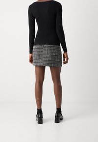 Top a maniche lunghe nero a coste abbinato a una mini gonna aderente e strutturata con un motivo monocromatico, completato da stivali neri alla caviglia.