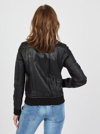 Schwarze Lederbomberjacke mit gerippten Bündchen und Saum, mit Nahtdetails und klassischer Passform. Trägt man über hellblauen Jeans.