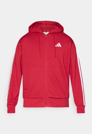 Piros cipzáras kapucnis pulóver húzózsinóros kapucnival, fehér díszítésekkel az ujjakon és hímzett logóval a bal mellrészen. Puha, sima anyagból.