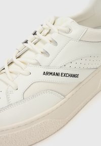 Weiße Leder-Sneaker mit durchbrochenem Design, kontrastierenden Stoffakzenten und einer strukturierten Sohle. Mit markiertem Logo und flachen Schnürsenkeln.