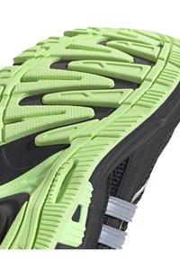 Svart sportskosula med en grön, texturerad gummiyttersula som har framträdande greppriller och grå accenter på den övre delen.