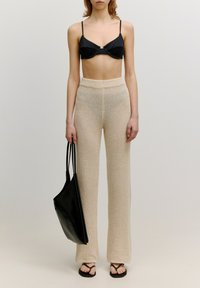 Zwarte onderbewerkte bralette, crèmekleurige gebreide wijde broek en zwarte totebag. Zachte textuur, lichtgewicht materiaal, minimalistisch ontwerp.
