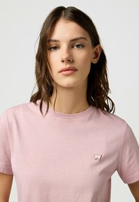Lyserød bomulds T-shirt med klassisk rund halsudskæring. Har et lille broderet logo på venstre bryst. Blød tekstur og korte ærmer.