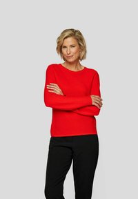 Roter gerippter Strickpullover mit langen Ärmeln und Rundhalsausschnitt, kombiniert mit schwarzen Hosen. Schlichtes Design ohne sichtbare Muster oder Beschläge.