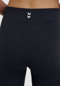 Czarne legginsy sportowe o gładkiej fakturze i wysokim stanem. Zawierają trzy białe chevrony z tyłu, wskazujące na szczegóły marki.