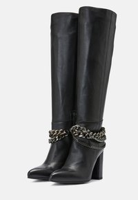 Mustat nahka polvipituiset saappaat, joissa on terävä kärki, tukeva korko ja koristeellinen hopeaketju nilkan ympärillä.