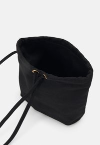 Czarna torba materiałowa ze ściąganym wierzchem. Posiada dwa sznurki i metalowe oczka w złotym odcieniu. Miękka textura, prosty design i kompaktowy kształt.