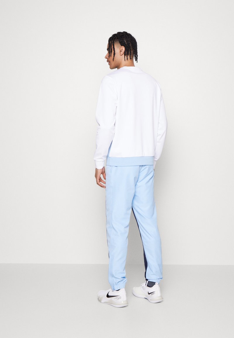 Sudadera blanca y joggers azul claro, con puños elásticos. Zapatillas deportivas blancas con acentos negros, vistas desde la parte posterior.