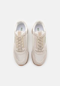 Sneakers atletiche beige con tomaia in rete e suede, suola in gomma testurizzata e lacci crema. Presentano un accento verde del logo sul lato.