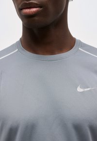 Close-up of a person wearing a light gray Nike sports shirt with a white swoosh logo on the chest and white stitch details on the shoulders.