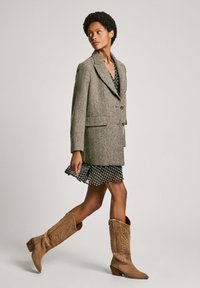 Hall herringbone blazer, mille kraega, nupuga kinnitamine ja kaks taskut, kantud musta kleidi peal, millel on valged täpid ja volangäär.