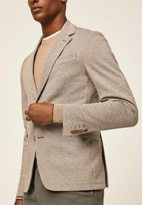 Hellbrauner gemusterter Blazer mit strukturierter Oberfläche, Ein-Knopf-Verschluss und drei braunen Knopf-Akzenten am Ärmelabschluss.